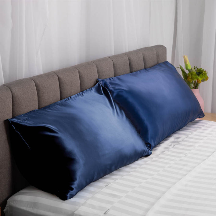 Two navy, plush silk pillows neatly laid on a modern bed, with a grey headboard.