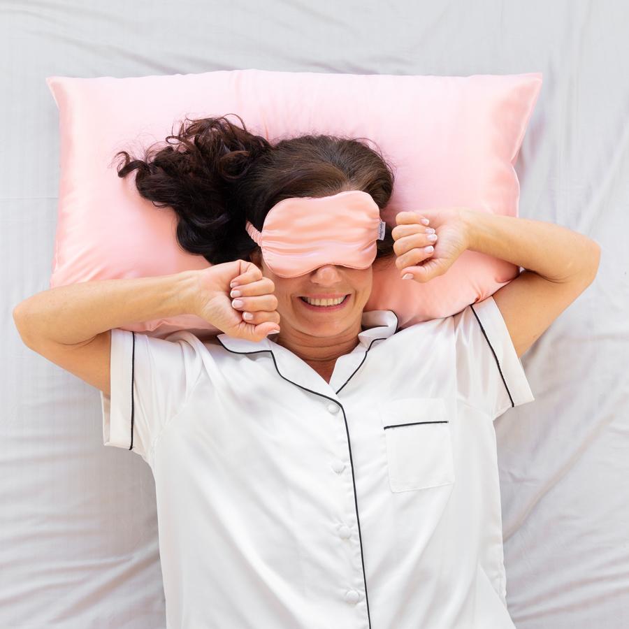 Woman with pink eye mask waking up with a smile after a well rested sleep.