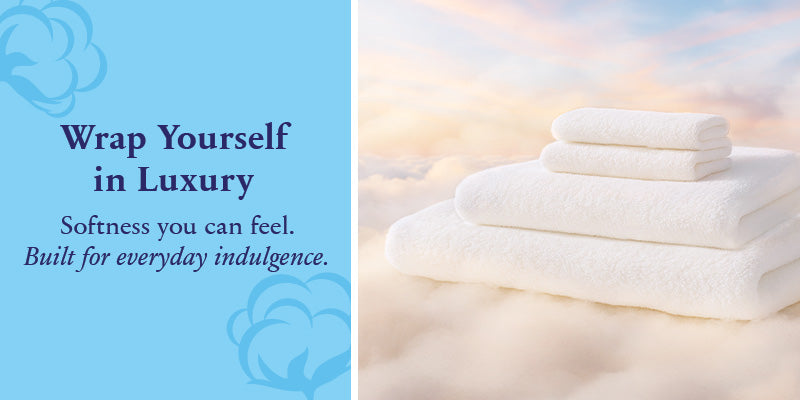 A stack of white towels is placed on a soft, cloud-like surface with a pastel sky background. Next to them is blue text that reads, Wrap Yourself in Luxury. Softness you can feel. Built for everyday indulgence.