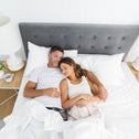 Couple sleeping in bed with a grey headboard and white covers