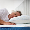 A middle-aged man with gray hair sleeps on his side, resting on a white pillow with blue circles. He enjoys extra comfort from the Super Sleeper Pro #1 Customer Choice Straight 2 Sleep® Mattress Topper with Cooling Technology and bonus free pillows.