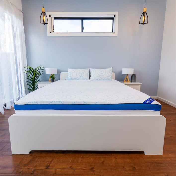 A modern bedroom features a white bed with the Super Sleeper Pro #1 Customer Choice Straight 2 Sleep® Mattress Topper with Cooling Technology and FREE pillows. White nightstands, small lamps, a plant, pendant lights, and a window complete the scene.