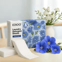 A box of Kleva Range Stain Lifting Laundry Detergent Sheets with a blue floral design sits on a table next to a vase of white and blue flowers. The eco-friendly detergent sheets, stacked beside the box, come in plastic-free packaging.