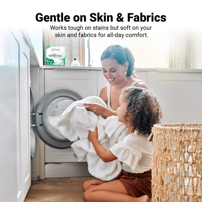 A woman and child kneel by a front-loading washer with white towels. Kleva Range Stain Lifting Laundry Detergent Sheets, Fresh Linen, offer eco-friendly, plastic-free laundry care—tough on stains, gentle on skin and fabrics.