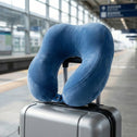 Portable blue travel pillow attached to suitcase at train station platform