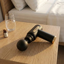 Portable cordless massage gun resting on table for home muscle recovery