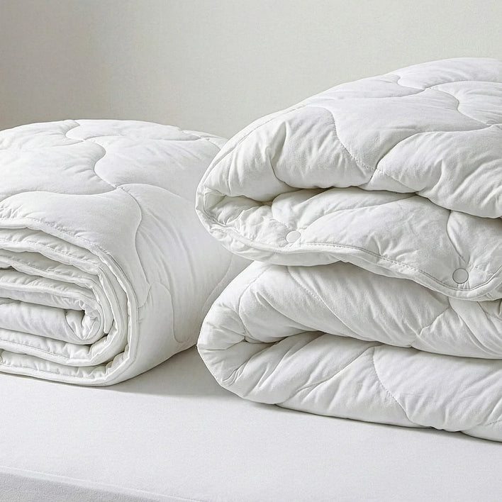 Three white, quilted comforters are neatly stacked, highlighting the coziness of the Super Sleeper Pro Quilt 365 All Season 2-in-1 Adjustable Quilt Set with two FREE luxurious Marshmellow Pillows for customizable comfort.