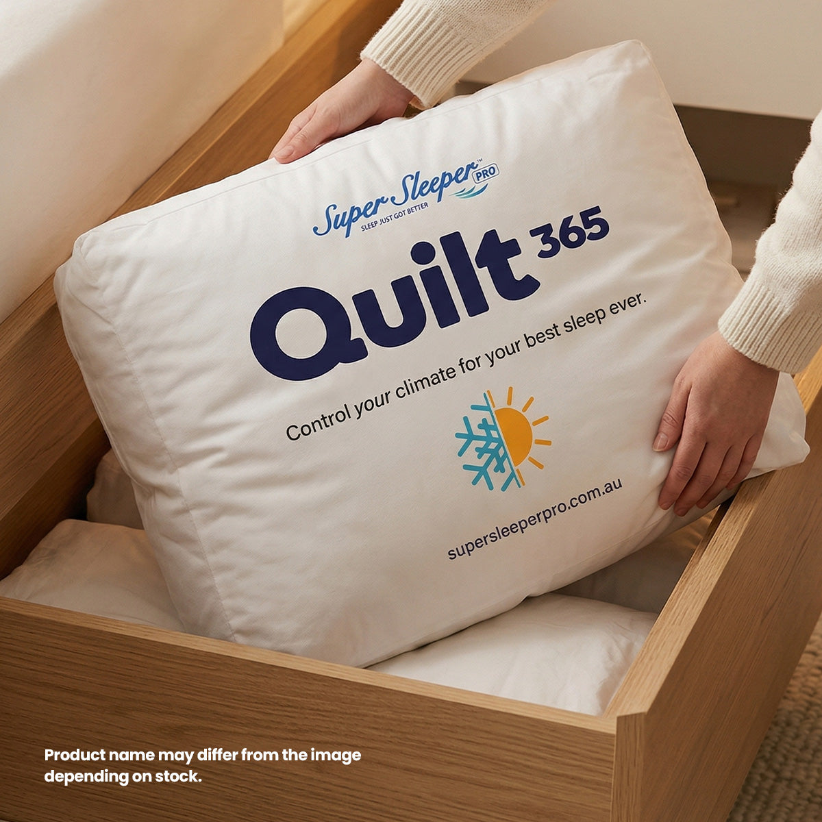 A person places a white Super Sleeper Pro Quilt 365™ All Seasons Two Plush Quilts pillow—featuring climate control icons and all-season branding—into a wooden drawer. Product name and a note about variation are visible on the pillow.