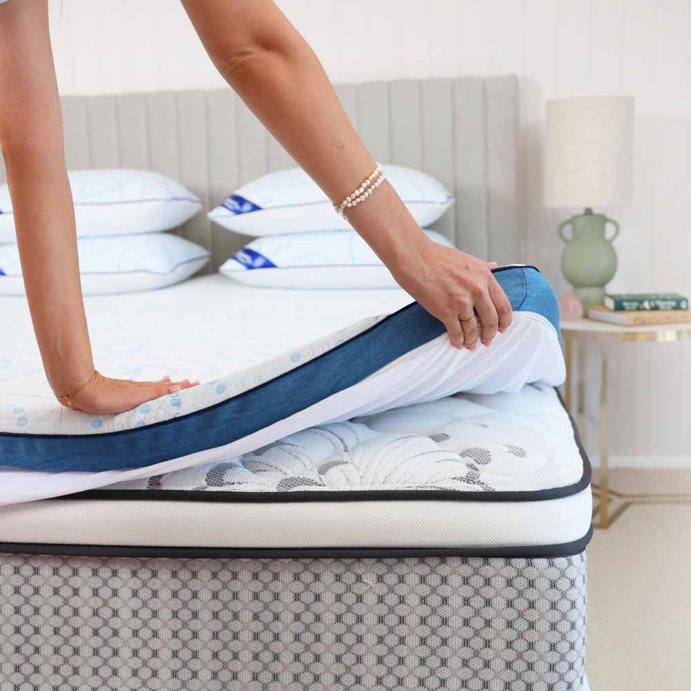 Person placing a mattress topper on top of their bed
