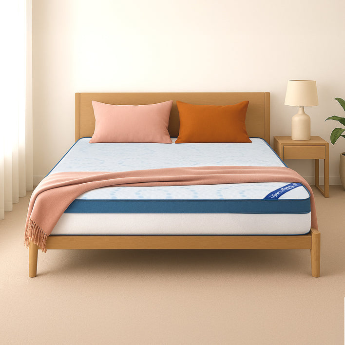 A tidy bed with a light wooden frame, pink and orange pillows, a salmon throw, and the Super Sleeper Pro [Queen] Straight 2 Sleep® Mattress Topper with Cooling Technology plus free pillows. A nightstand with a lamp and plant is on the right.
