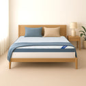 A minimalist bedroom with a light wood bed frame, blue and beige pillows, blue blanket, and white mattress topped by the Super Sleeper Pro [Double] Straight 2 Sleep® Mattress Topper with Cooling Technology + FREE Pillows. Lamp and plant on nightstand.