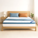 A simple, bright bedroom features a light wood bed with the Super Sleeper Pro [King] Straight 2 Sleep® Mattress Topper with Cooling Technology and FREE blue and orange pillows. A nightstand with a lamp and plant complete the hotel-like look.