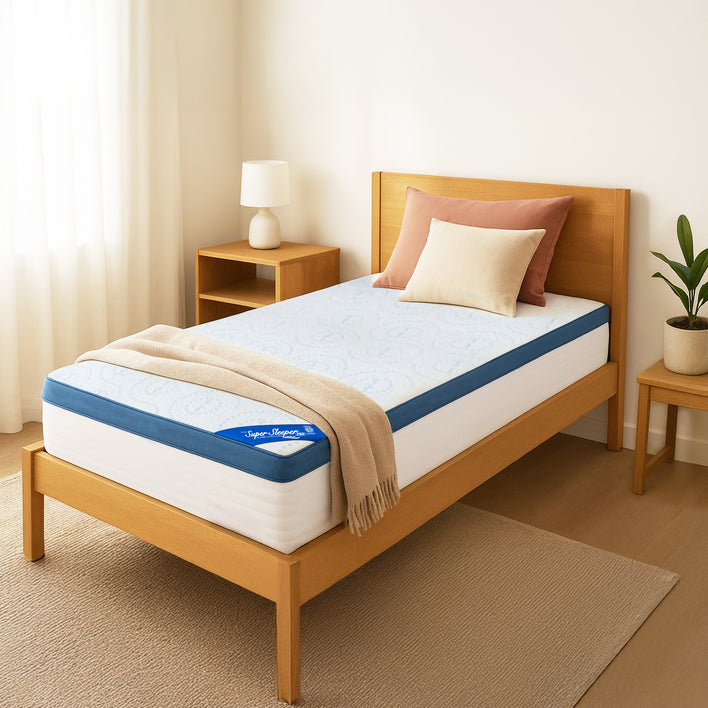 A neatly made twin bed with a light wood frame features a Super Sleeper Pro [Single] Straight 2 Sleep® Mattress Topper with Cooling Technology and free pillows. Nearby, a bedside table holds a lamp and plant, with neutral walls and white curtains.