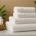 A neatly folded Royal Deluxe Dream 4pc Towel Set by Super Sleeper Pro sits on a marble surface next to a wicker basket and bottle, with green leaves against a beige wall. Get a FREE 2nd 4pc set—Sleep Just Got Better!.
