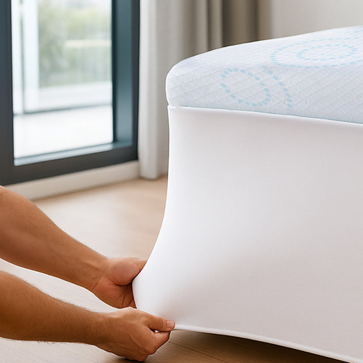 Person lifting a white mattress with blue pattern from a box near a window.