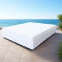 White mattress on a tiled floor with a blue ocean and sky in the background