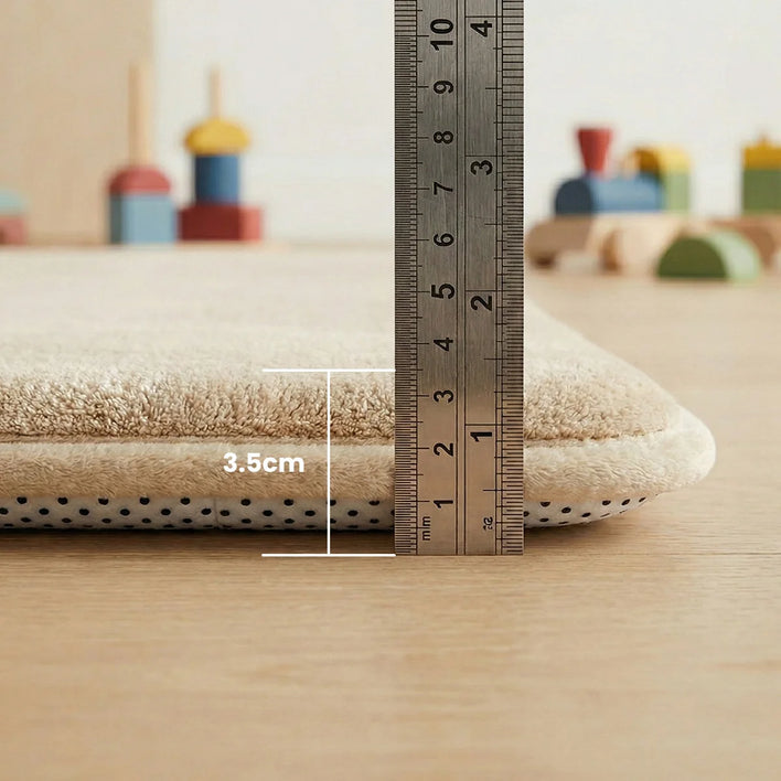 A metal ruler stands next to the Super Sleeper Pro Plush Soft Touch Sensory Tatami Mat, showing its 3.5 cm thickness. Beige mat looks like a rug, but works as a play mat; blurred wooden toys and light wood floor in the background.