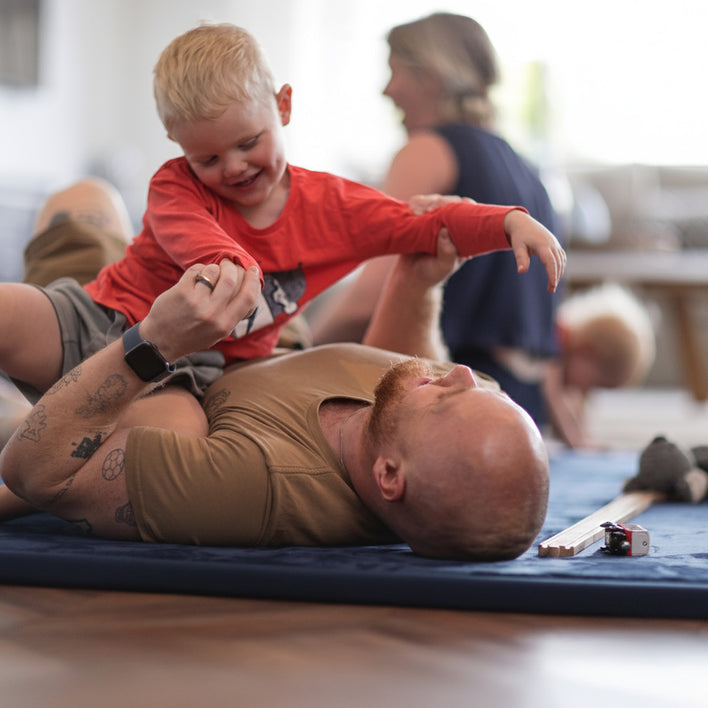 Child laughing and playing on a cushioned tatami floor mat while an adult lies beside them, showing a comfortable tatami mat floor surface.
