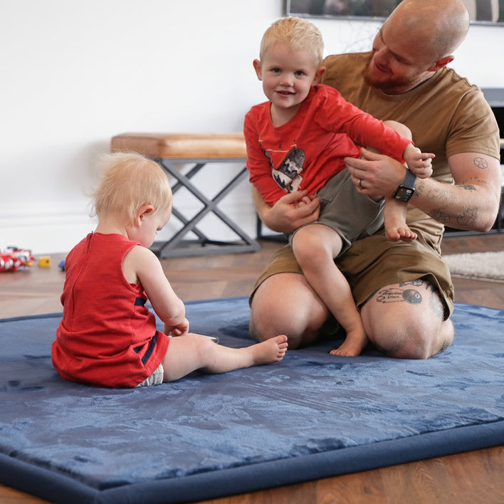 Two young children and an adult sitting and playing on a thick tatami floor mat, highlighting a safe and padded floor tatami mat for families.