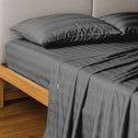 A neatly made bed features the Super Sleeper Pro Buy 1 Get 1 FREE: Royal Deluxe Imperial Dream Sheets™ Cotton Sateen 1200TC 4pc Bedding Set in dark gray stripes, with matching pillows and a light gray upholstered headboard.