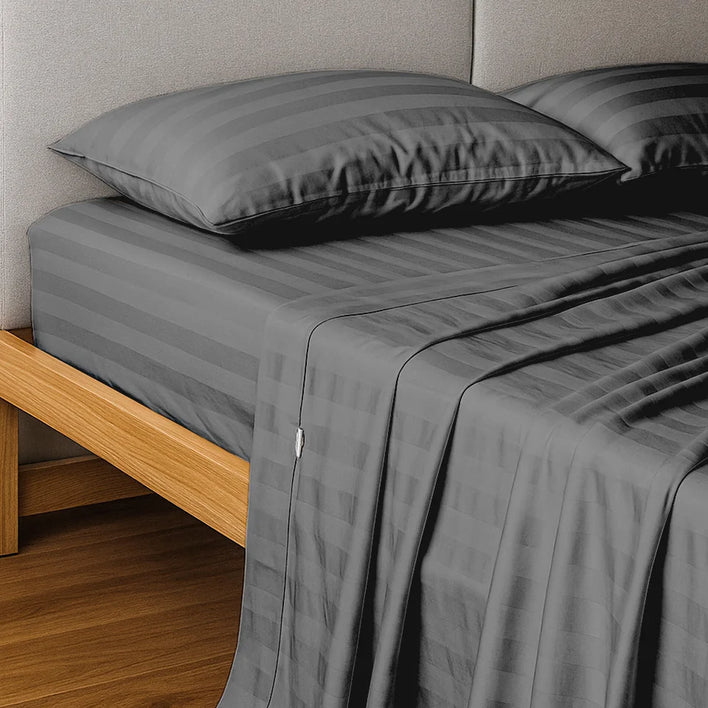 A neatly made bed features the Super Sleeper Pro Buy 1 Get 1 FREE: Royal Deluxe Imperial Dream Sheets™ Cotton Sateen 1200TC 4pc Bedding Set in dark gray stripes, with matching pillows and a light gray upholstered headboard.