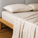 A neatly made bed features Super Sleeper Pro’s Buy 1 Get 1 FREE: Royal Deluxe Imperial Dream Sheets™ Cotton Sateen 1200TC 4pc Set, draping elegantly over a light wooden frame with two matching pillows, against a gray padded headboard. Free organiser bands included.