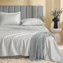 A neatly made bed features Super Sleeper Pro’s Buy 1 Get 1 FREE Royal Deluxe Imperial Dream Sheets™ Cotton Sateen 1200TC set in light gray stripes, with a textured gray blanket, upholstered headboard, and a side table with eucalyptus branches.