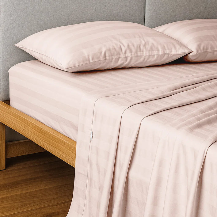 A neatly made bed featuring Super Sleeper Pro’s Buy 1 Get 1 FREE Royal Deluxe Imperial Dream Sheets™ Cotton Sateen 1200TC 4pc Bedding Set in light pink stripes, with pillowcases and free organiser bands on a wooden frame against a grey headboard.