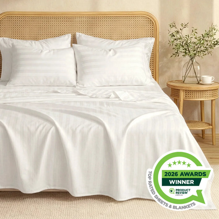 A neatly made bed features Super Sleeper Pro Buy 1 Get 1 FREE: Royal Deluxe Imperial Dream Sheets™ Cotton Sateen 1200TC 4pc Set + Free Organiser Bands. Two pillows rest against a rattan headboard; a table with a vase and grass is nearby. Awarded Winner 2026.