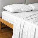 A neatly made bed with Super Sleeper Pro’s Royal Deluxe Imperial Dream Sheets™ 1200TC cotton sateen set, plus free organiser bands, on a wood bed frame and light gray upholstered headboard atop a wooden floor.