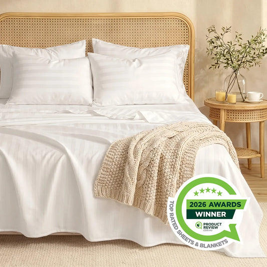 A neatly made bed with Super Sleeper Pro Royal Deluxe Imperial Dream Sheets™ Cotton Sateen 1200TC 4pc Set, a beige knitted blanket, four pillows, a nightstand with books and vase, plus a 2026 Awards Winner badge in the foreground.