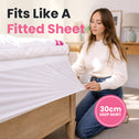 A woman kneels beside a bed in a bright bedroom, pulling out a fitted sheet. Large text reads 'Fits Like A Fitted Sheet' and a pink circle says '30cm DEEP SKIRT'.