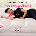 A woman lies on a white quilted mattress topper or bed pad in a bright bedroom setting, with promotional text reading 'UP TO 10CM OF PLUSH COMFORT' and a size callout indicating up to 10cm thickness.