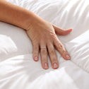 A hand with a simple ring presses down on the Super Sleeper Pro Marshmellow™ Plush Mattress Topper, highlighting its soft, quilted hotel-style texture and luxurious comfort.