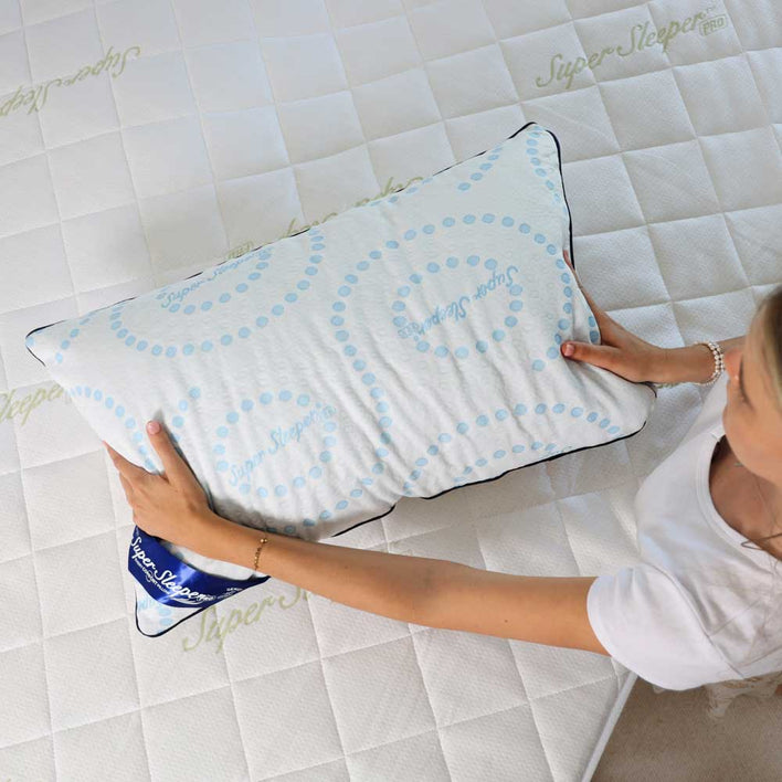 A woman holding a plush memory foam pillow on top on a white mattress