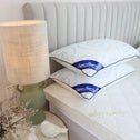 A bedside table with a green lamp and white decorative birds stands next to a bed with a tufted headboard. The Super Sleeper Pro Best Selling Every Comfort Pillow With Cooling Technology is stacked on the white quilted mattress for restful sleep.