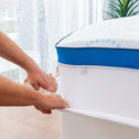 Hands securing mattress topper onto bed