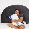 Man sitting on an additional layer onto the bed for extra comfort and support while hugging a pillow