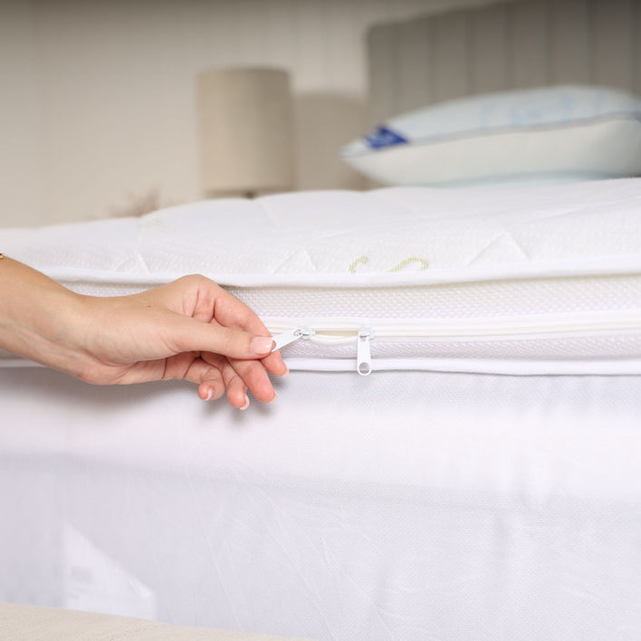 A hand using a zipper to fasten a cover onto a bedding accessory designed to enhance the comfort of a mattress