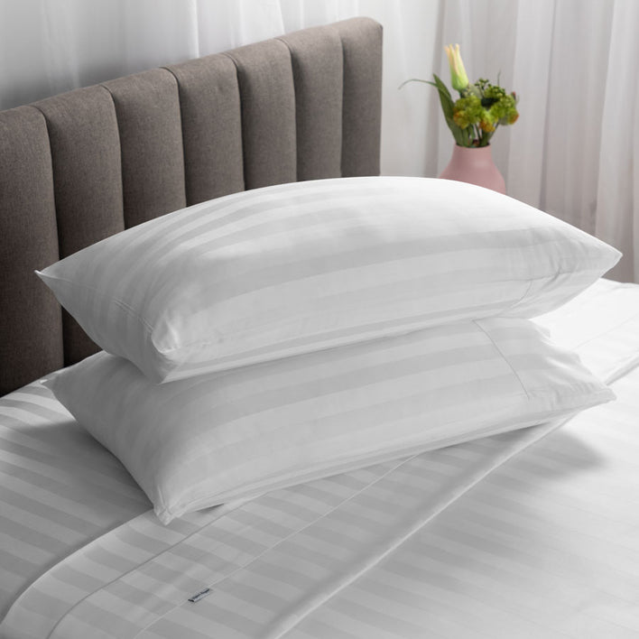 Two cosy pillows arranged neatly on a soft white bed, stacked on top of each other.