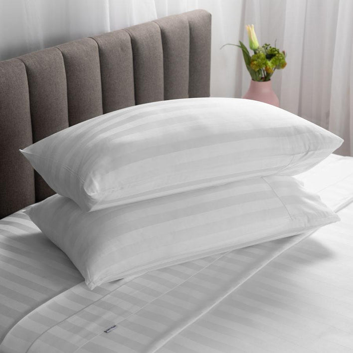 Two white, luxury pillows placed neatly on top of each other, while on a soft, white bed.