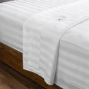 A sleek, white, weave bed sheet draped over a trendy wooden bed frame.