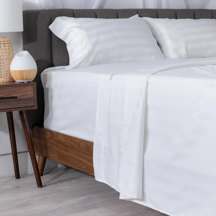 The left side of a dark wooden bed with luxury white bed linen draping over the side of the bed frame.