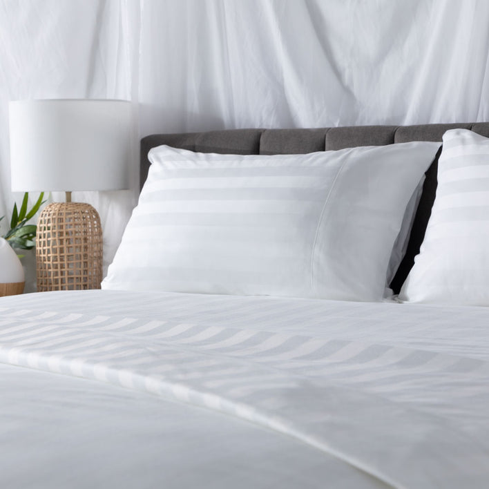 A smooth, white bed featuring Weave bedsheets and two comfortable, sleek pillows.