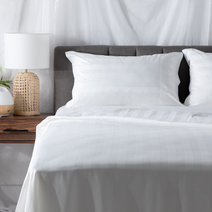 The left side of a well-made bed with comfortable white sheets and a wicker table lamp.