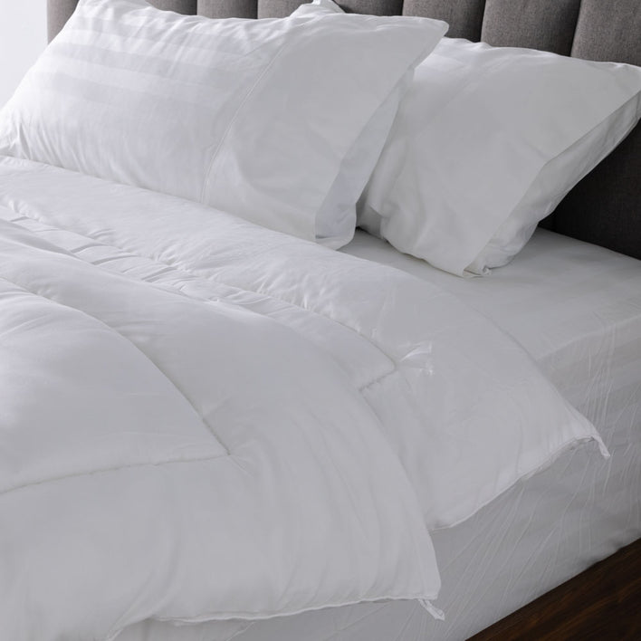 A large bed is accompanied by two soft, white pillows that are complemented by a matching soft, white quilt cover.