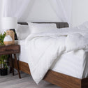A soft, white quilt cover draped over a wooden bed frame in a well-lit bedroom.