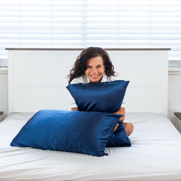 A lady sat in bed with two silk navy pillows