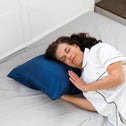 A dark haired lady laying comfortably with s navy plush pillow under her head.