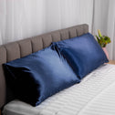 Two navy, plush silk pillows neatly laid on a modern bed, with a grey headboard. 